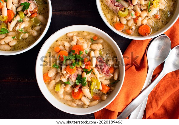 Bowls of White\
Bean and Ham Soup with Bread: Three bowls of cannellini bean soup\
with smoked pork and\
vegetables