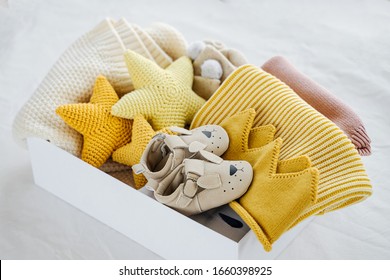 Box with baby stuff and accessories for newborn on bed. Gift box with knitted blanket, clothes, socks, shoes and toy. Baby shower concept.  Flat lay, top view - Shutterstock ID 1660398925