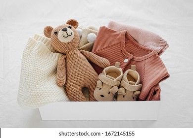 Box with baby stuff and accessories for newborn on bed. Gift box with knitted blanket, clothes, socks, shoes and toy. Baby shower concept.  Flat lay, top view