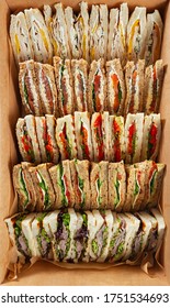 Box with club sandwiches for catering delivery top view.Delicious natural snacks for event venue meal delivered in big cardboard box.Triangle sandwich snack with red salmon fish,green salad for dinner