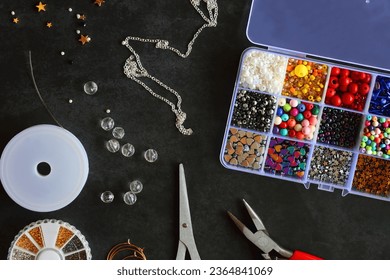Box with colorful beads, string, wire, chain, scissors, pliers and hammer on dark background. Various jewelry making supplies. Top view. - Shutterstock ID 2364841069