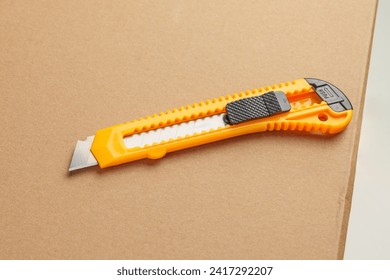 Box cutter on a parcel cardboard box close up. Retractable utility knife