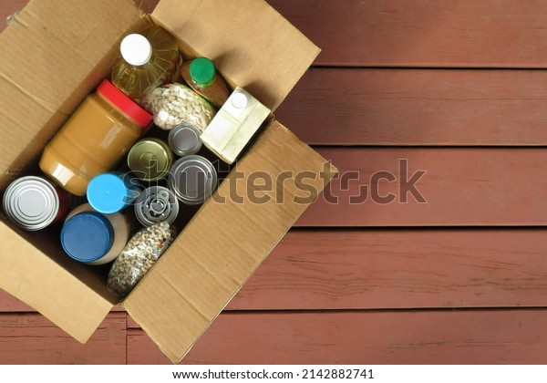 A box of donated canned goods and non-perishable\
foods for a food pantry for the poor sitting on red, wood panel\
background.  Copy space.