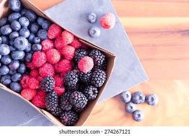 Box of fresh seasonal autumn berries with blueberries, blackberries, and raspberries displayed in a punnet on a wooden table fresh from the farmers market, with copy space
