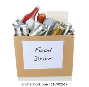 A Box Full Of Canned And Packaged Foodstuff For A Charity Food Donation Drive. Isolated On White With Reflection. Cans Have No Labels And The Box Has A Hand Made Sign.