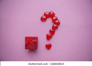 A box with a gift and a number of question marks laid out from small red hearts. Concept for Valentine's Day or another love event. A question mark means a surprise.