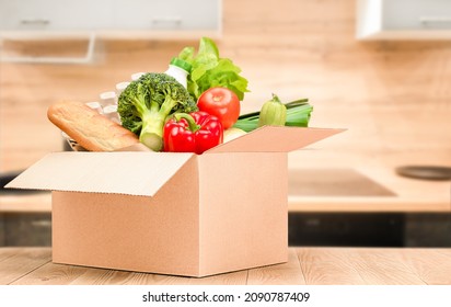 Box With Groceries On A Wooden Table Against The Background Of The Kitchen, Home Delivery