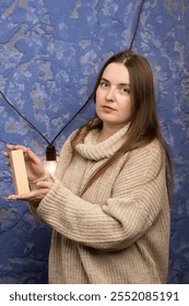 A box held by hands in front of a blue textured wall with a string of lights. Ideal for stock photos featuring home decor, gift packaging, and intimate, cozy themes.
