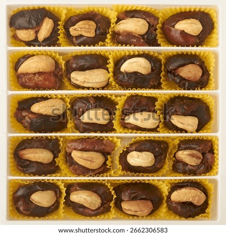 box of premium dates each stuffed with cashew nut, neatly arranged in rows and columns inside rectangular tray, placed in yellow paper liner, middle eastern desserts or ramadan treats