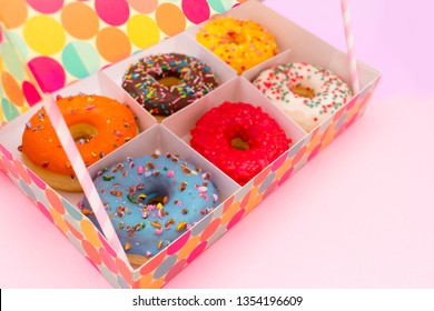 BOX WITH SIX COLORFUL DONUTS ON A SOFT PINK BACKGROUND 
