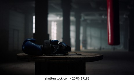 Box sport concept. Closeup boxing gloves lying on wooden box in empty gym. Fitness equipment in sport club. Modern gym with punching bag for boxing training on background.  - Powered by Shutterstock