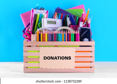 Box with various school and office supplies with a sign on a bright blue background. Donation concept