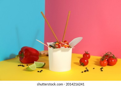 Box Of Vegetarian Wok Noodles With Ingredients And Chopsticks On Color Background