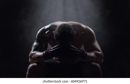 Boxer athlete sits with a drooping head on a black background