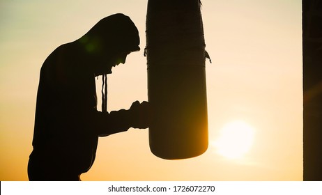 Boxer beats punching bag on sunset background. Silhouette motivation sport boxing. Martial arts. Training in the fresh air. - Powered by Shutterstock