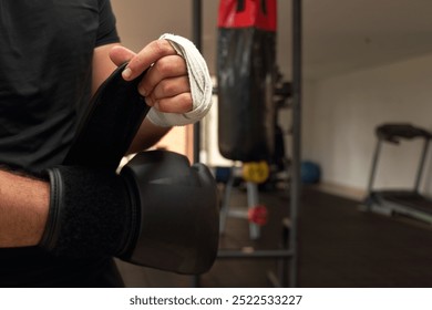 Boxer in a gym wrapping his hands with white bandages, adjusting his black gloves before a training session the preparation ensures safety and protection for his hands during intense punching drills - Powered by Shutterstock