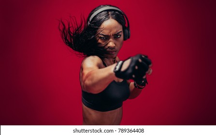 Boxer practicing her punches in a studio. African female boxer practicing boxing against red background. - Powered by Shutterstock