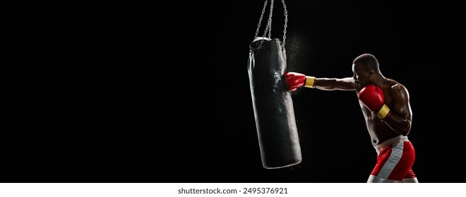 Boxer in red gloves delivering powerful punch to a heavy bag isolated on black background isolated on black background. Concept of sport, active lifestyle, strength. Banner. Copy space for ad, text - Powered by Shutterstock