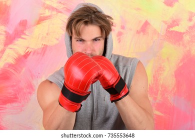 Boxer with serious face trains to hit. Man with messy hair on colorful background. Sports, box and fight concept. Guy in grey sleeveless hoodie wears red leather boxing gloves - Powered by Shutterstock