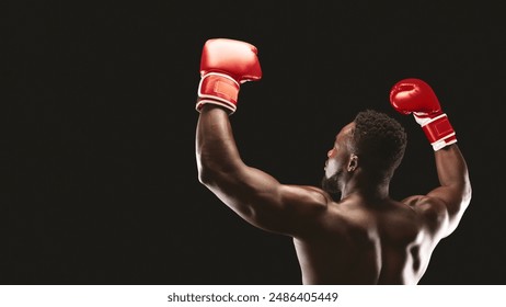 A boxer wearing red gloves raises his arms in victory against a black background. - Powered by Shutterstock