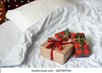 Boxes With Christmas Gifts On The Bed With A White Blanket And Pillow. The Bedroom Is Decorated With Christmas Lights. 