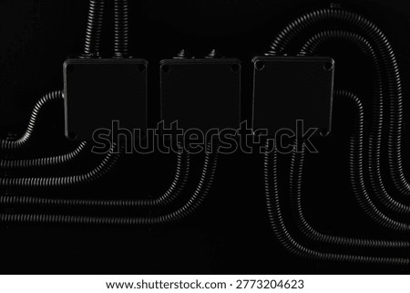 Boxes and electrical cable conduits hanging on black wall Industrial electrical conduits and junction boxes aligned on dark wall interior