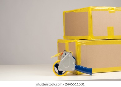 Boxes and tape on white table. Parcels with yellow tape on corners. Packaged goods are ready to be shipped. Parcels to be sent via delivery services. Boxes for long-term storage. Packaging materials