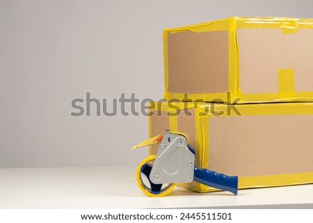 Boxes and tape on white table. Parcels with yellow tape on corners. Packaged goods are ready to be shipped. Parcels to be sent via delivery services. Boxes for long-term storage. Packaging materials