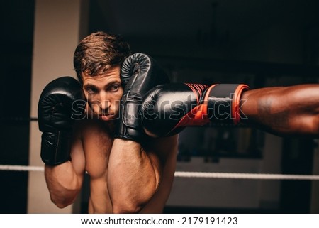 Boxing athlete blocking a punch to his jaw during a match with his opponent. Two male boxers fighting in a boxing ring.