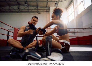 Boxing coach and female fighter getting ready for sports training while wrapping hand with a bandage.  - Powered by Shutterstock