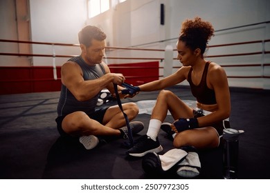 Boxing coach wrapping sportswoman's hands with bandage before training in health club.  - Powered by Shutterstock