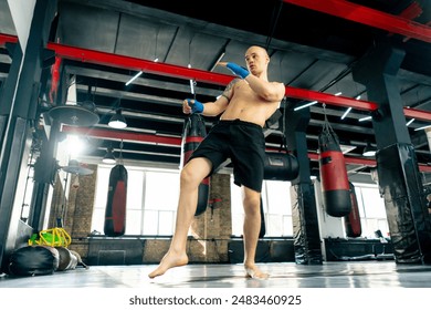 in a boxing fight club bald young boxer with tattoos in blue bandages trains a kick before a fight professional training fighting technique training - Powered by Shutterstock