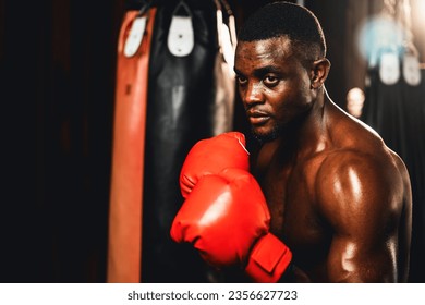 Boxing fighter shirtless posing, African American Black boxer wearing red glove in defensive guard stance ready to fight and punch at gym with kick bag and boxing equipment in background. Impetus - Powered by Shutterstock