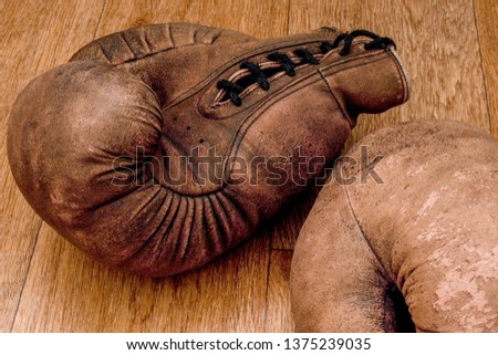 Boxing gloves. Old vintage retro pair of leather worn mittens are on the wood table. Red colors and soft lights. Gloves of retired boxer and fighter