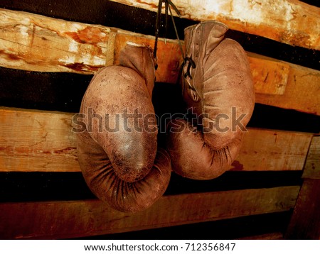 Boxing gloves on the wall. Old, vintage pair of leather mittens hangs on the wood wall. Red colors and soft lights. Gloves of retired boxer and fighter. It hangs on a nail in a barn or rustic house.