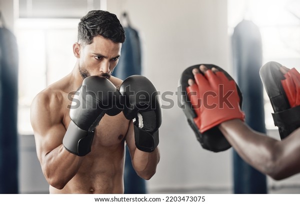 Boxing gym, fighting pad and man training with
athlete coach for a fitness cardio exercise session. Strength,
focus and fighter workout for punch technique with professional
sports equipment.