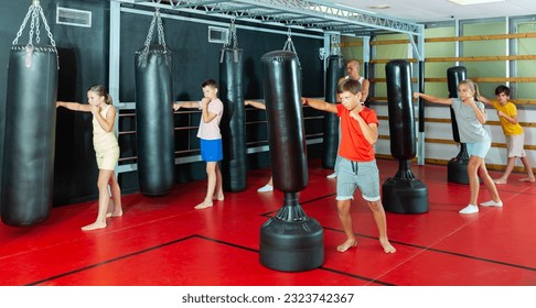 Boxing instructor and young preteen children practicing blows on the punching bags during training at gym