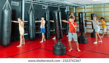 Boxing instructor and young preteen children practicing blows on the punching bags during training at gym