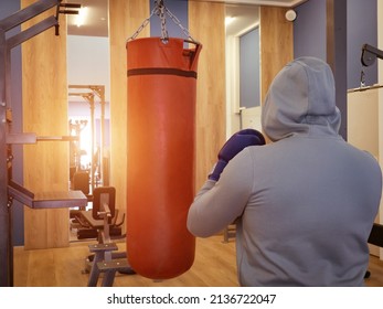 Boxing Training - A Hand And A Red Punching Bag.a Guy In A Hood Hits A Punching Bag