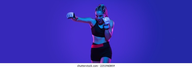 Boxing. Young woman athletic female MMA fighter training isolated on gradient blue-pink background in neon light. Concept of sport, competition, action, healthy lifestyle. Banner for ad - Powered by Shutterstock