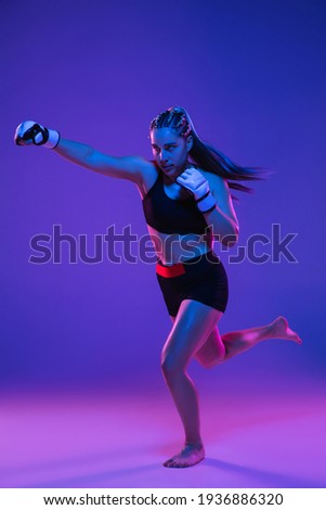 Boxing. Young woman athletic female MMA fighter training isolated on gradient blue-pink background in neon light. Concept of sport, competition, action, healthy lifestyle. Copy space for ad.