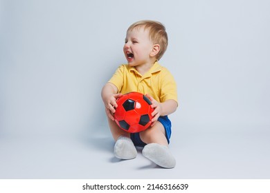 Boy 3-4 years old football fan in a yellow T-shirt with a ball in his hands, holding a soccer ball in his hands, isolated on a white background. The concept of sports family recreation