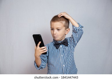 Boy 3-6 Years Old In A Shirt In A Cage Is Puzzled Looking At The Phone. An Interrupted Conversation. Middle Plan