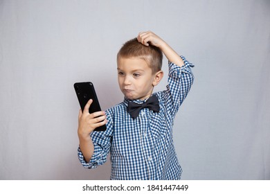 Boy 3-6 Years Old In A Shirt In A Cage Is Puzzled Looking At The Phone. An Interrupted Conversation. Middle Plan