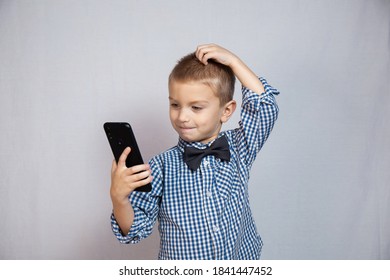 Boy 3-6 Years Old In A Shirt In A Cage Is Puzzled Looking At The Phone. An Interrupted Conversation. Middle Plan