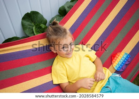 boy of 5 years old sits on a multi-colored hammock, plays with a toy Pop It in the shape of a heart. The child is on vacation. trendy entertainment for children with a relaxing effect