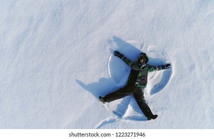 Boy Of 7 Years Makes Snow Angel In Snow Area. Aerial Foto.