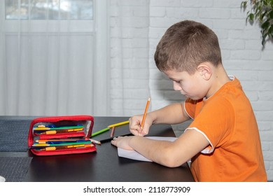 A boy of 7-10 years old draws with colored crayons at the table.
