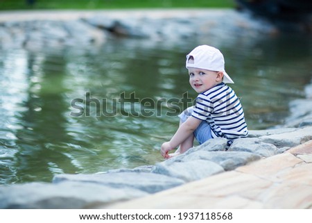 Boy in admiration and joy is sitting on the edge of a pond  and washes feet in the water