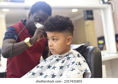 Boy in the african barbershop. Cute mixed boy makes a haircut in the African salon. Hair style. Haircut by machine for children. School boy hair style. Haircut by scissors. 